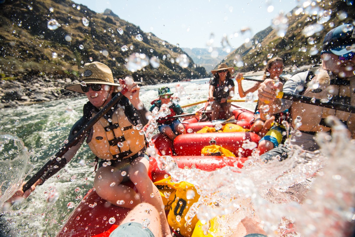  People in a raft navigate the rapids of a river with large waves splashing over the edge.